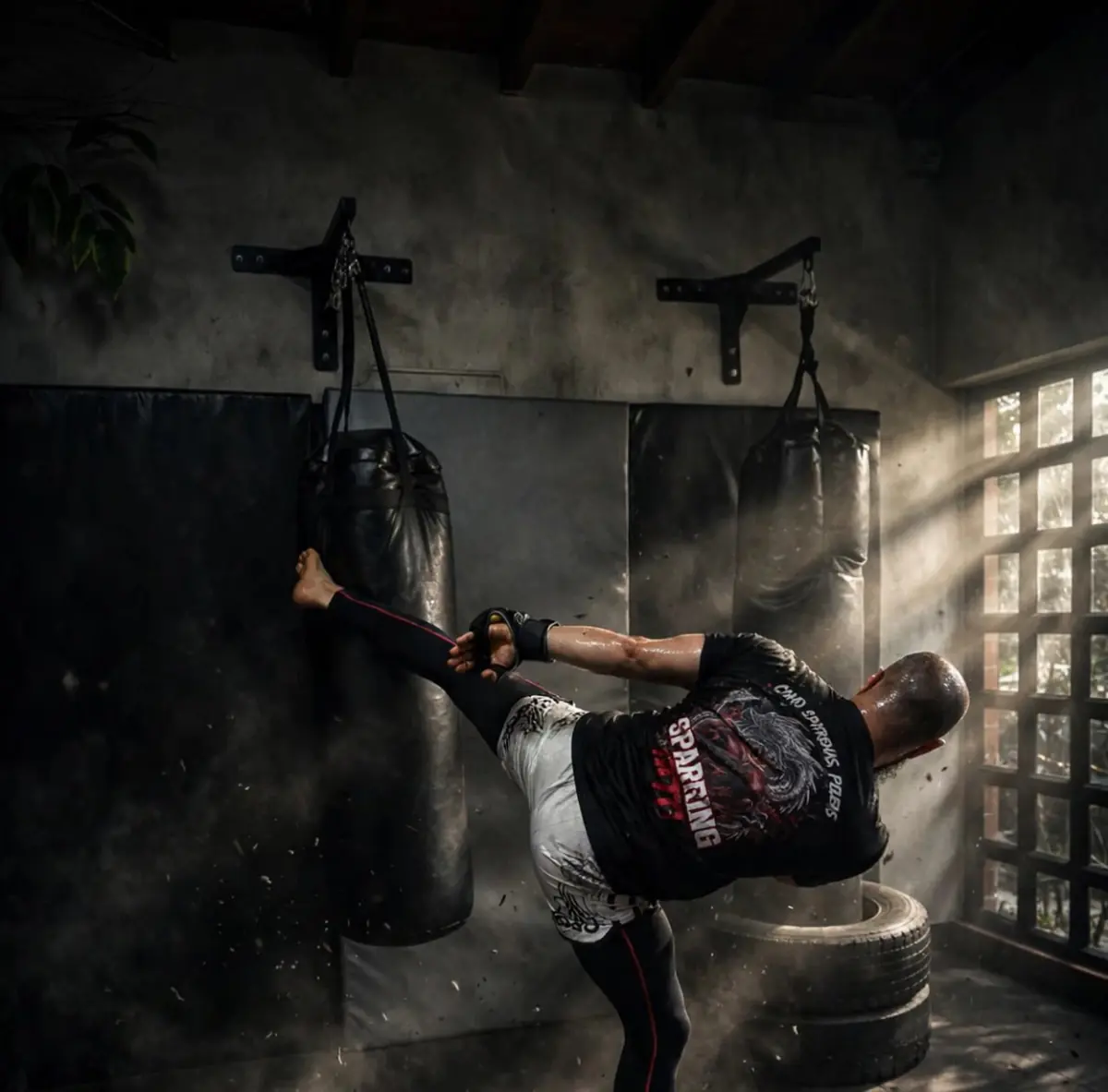 Peleador lanzando una patada alta al saco de boxeo en el dojo, con luz entrando por la ventana